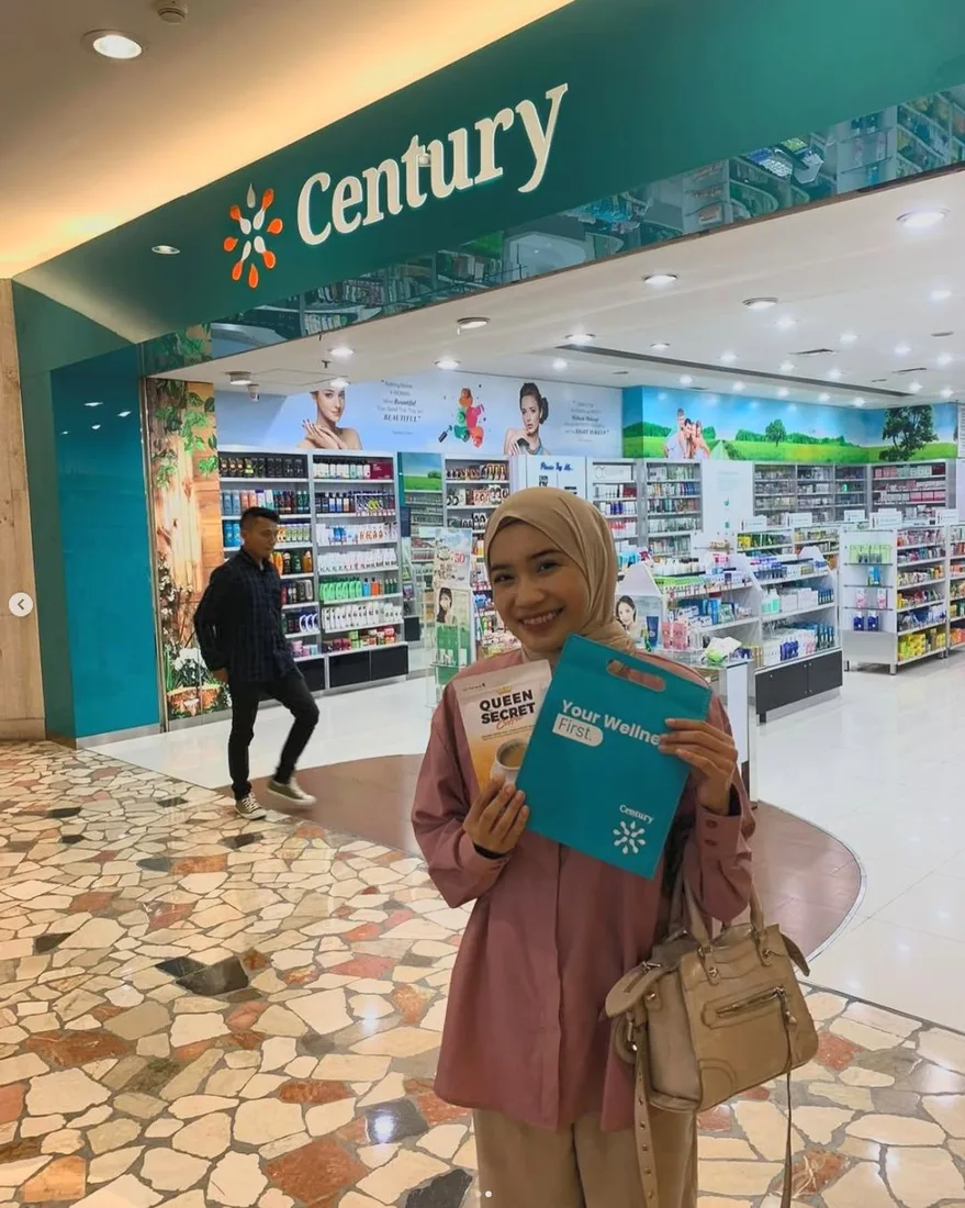 Pelanggan QSC memegang kemasan Queen Secret Coffee dan tas belanja di depan apotek Century dalam mall